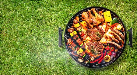 Top view of assorted delicious grilled meat with vegetables on barbecue grill with smoke and flames in green grassの写真素材