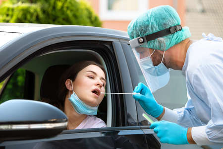 Woman getting tested at a coronavirus drive thru station by medical staff with PPE suit by throat swab. Health care drive thru service and medical conceptの写真素材