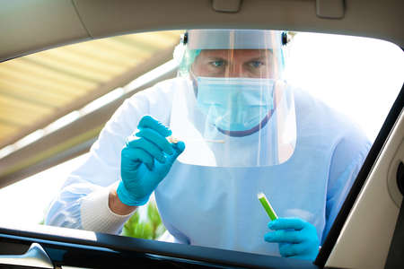Medical staff with PPE suit testing patient at a Covid-19 drive thru by throat swab. Health care...