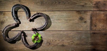 Four leaf clover made out of old rusty horse shoes as symbol for lucky charm on rustic wooden backgroundの写真素材