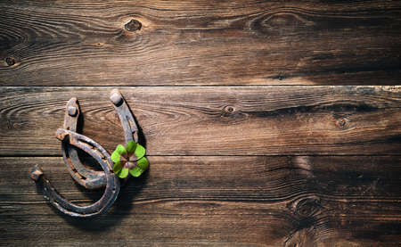 Two old rusty horse shoes and four leaf clover as symbol for lucky charm on a rustic wooden backgroundの写真素材