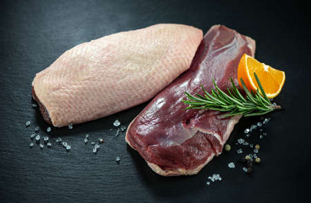 Raw duck breast pieces garnished with rosemary and orange slices on dark slate backgroundの写真素材