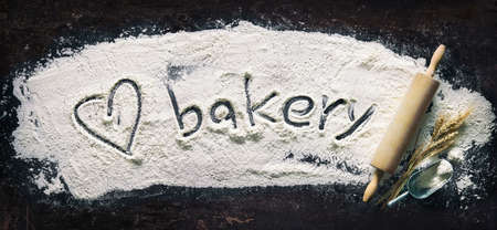 Baking background with a heart shape and text Bakery handwritten in flour and rolling pin on dark tableの写真素材