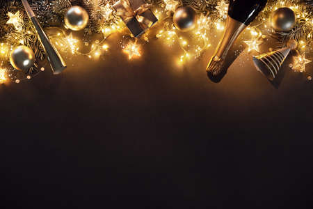 Christmas and New Years holidays background with fir branches, christmas balls, champagne bottle, gift box and lights on dark boardの写真素材