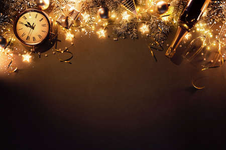 New Years Eve holiday background with fir branches, clock, christmas balls, champagne bottle, gift box and lights on dark boardの写真素材