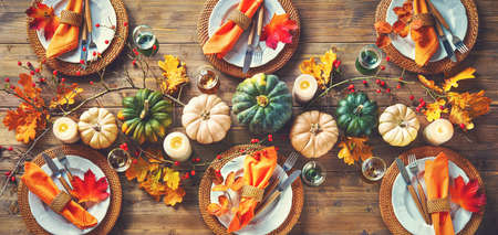 Autumnal decorated table for celebrating Thanksgiving or other family celebration. Festive table setting with plates, glassware, pumpkins, rose hip branches and leaves on wooden table background, top viewの写真素材