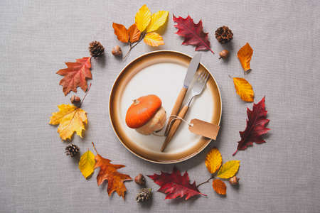 Thanksgiving autumn table setting with cutlery and arrangement of colorful fall leaves and pumpkinの写真素材