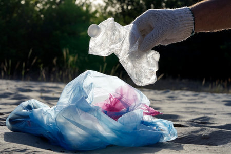 Plastic pollution in the environmental problem of the world. A hand in a white glove puts garbage in a plastic bag. Removal and cleaning of garbage from contaminated territoriesの写真素材