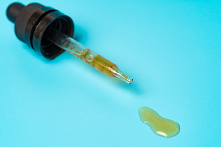 Pipette with spilled yellow liquid on a blue background used for medical and cosmetic purposesの写真素材