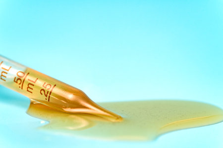 Pipette with spilled yellow liquid on a blue background used for medical and cosmetic purposesの写真素材