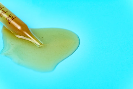 Pipette with spilled yellow liquid on a blue background used for medical and cosmetic purposes