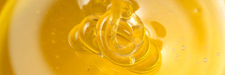 Honey drips from a wooden honey dipper on a yellow background. Sweet bee product for your design...