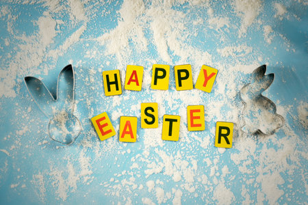 Multicolored letters laid out in the word Easter on a blue background with a baking mold in the...