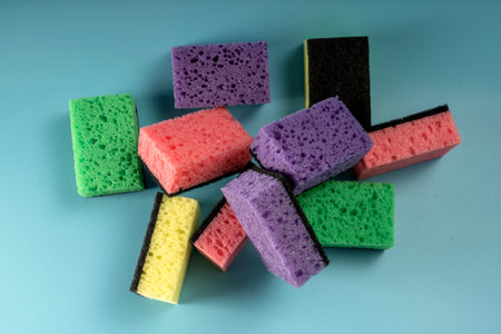 Multicolored sponges for washing dishes and other household needs. The sponges lie on a blue background at a slight angle. Cleaning and Dishwashing Conceptの写真素材