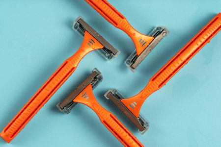 Plastic razor on blue background. The concept of using a razor. Razor device. The concept of skin care. Epilation hair removal. Orange men's shaving razors, top view.の写真素材
