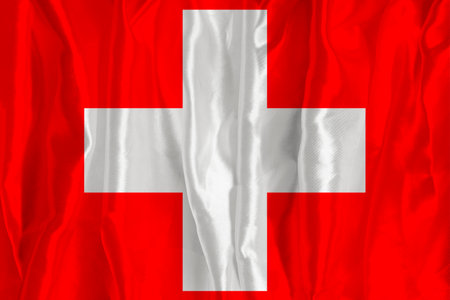 The Swiss flag on a silk background is a great national symbol. Texture of fabrics The official state symbol of the countryの写真素材