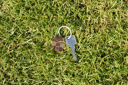 House keys with a keychain in the shape of a house on green grassの写真素材