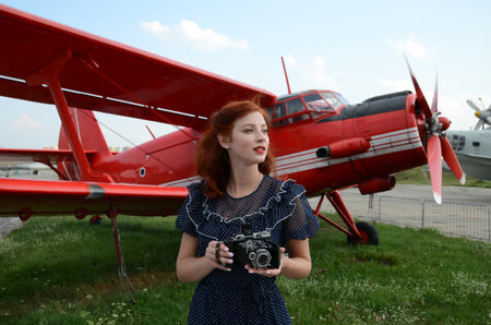 A beautiful girl with red wavy hair and red lipstick on her lips in a blue dress with white polka...