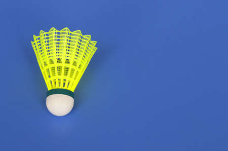 A bright yellow shuttlecock for playing badminton lies on a blue backgroundの写真素材