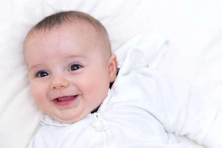 HAPPY BABY. Beautiful and little baby boy happy and smiling resting on the bed.
