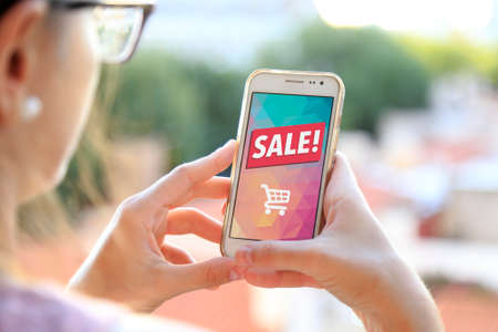 Girl holding a smartphone a sale advertising on the screen. Marketing, discount, internet, cell phone publicity.の写真素材