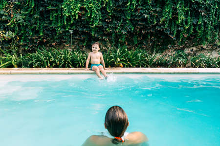 Little boy jumping into a pool. Child get fun in the swimming pool of his home. Outdoors activities in quarantine.の写真素材