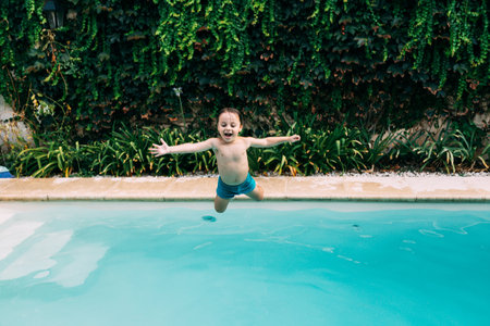 Little boy jumping into a pool. Child get fun in the swimming pool of his home. Outdoors activities in quarantine.の写真素材
