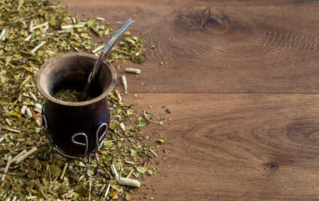 Traditional mate made of calabash over a wooden table with yerba mate scattered over it.