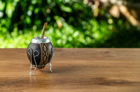 Traditional Argentine Mate made of pumpkin and lined in leather on a wooden table in the open air....