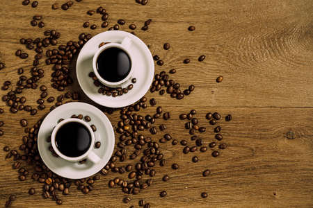 Top view of two white coffee cup over a wooden table with scattered coffee beans.