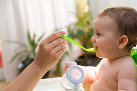 Adorable baby eating food. His mother feeds him with a spoon.の写真素材