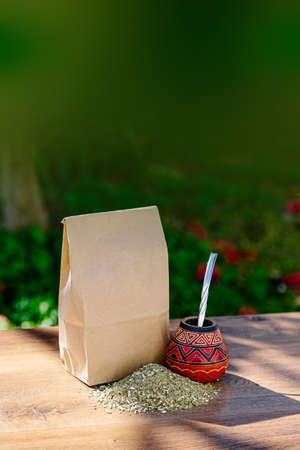 A rustic pack of brown paper with a traditional mate made of calabash over a wooden table with yerba...