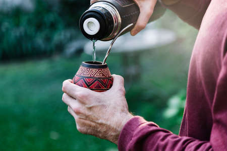 Man preparing a mate with hot water. Gourd mate with yerba inside. Middle age latin american man enjoying at the sunset outdoors.の写真素材