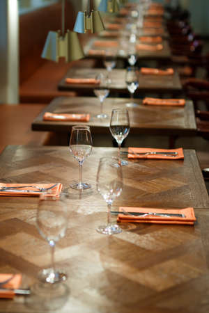 wooden table served with plates, forks, spoons, glasses, napkins in the restaurant