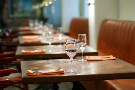 wooden table served with plates, forks, spoons, glasses, napkins in the restaurant