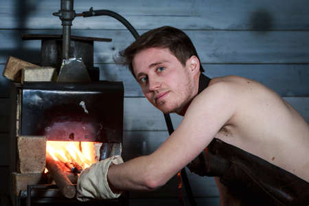 Blacksmith forging the molten metal on the anvil in smithy.