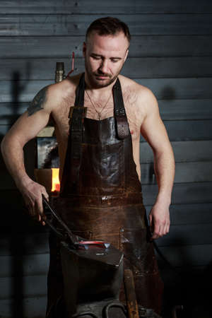 portrait of a young handsome blacksmith at work in his forgeの写真素材