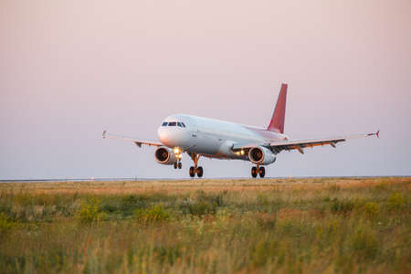 white Passenger airplane landing at sunset on a runway. sunset. pink, blue, yellow skyの写真素材