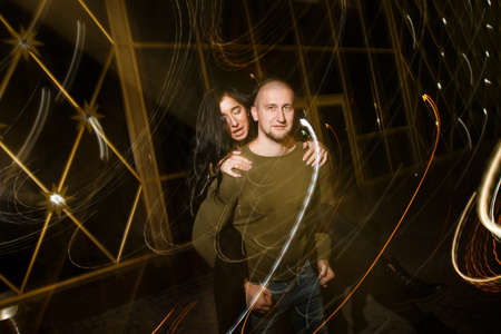 young stylish modern couple of young beautiful women wiht long dark hair and handsome man are kissing, have fun, jocking, hugging, laughing on the street at nightの写真素材