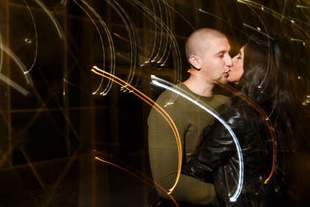 young stylish modern couple of young beautiful women wiht long dark hair and handsome man are kissing, have fun, jocking, hugging, laughing on the street at nightの写真素材