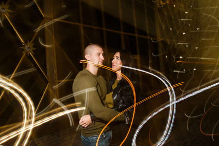 young stylish modern couple of young beautiful women wiht long dark hair and handsome man are kissing, have fun, jocking, hugging, laughing on the street at nightの写真素材