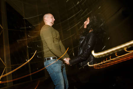 young stylish modern couple of young beautiful women wiht long dark hair and handsome man are kissing, have fun, jocking, hugging, laughing on the street at nightの写真素材