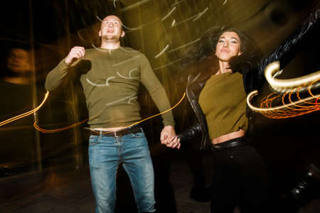 young stylish modern couple of young beautiful women wiht long dark hair and handsome man are kissing, have fun, jocking, hugging, laughing on the street at nightの写真素材