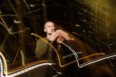 young stylish modern couple of young beautiful women wiht long dark hair and handsome man are kissing, have fun, jocking, hugging, laughing on the street at nightの写真素材