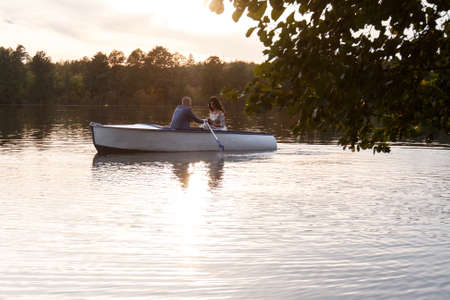 beautiful young wedding couple,bride with flower and her groom just married on small boat at pond with evening sun.happy loving couple rowing a small boat on a lake.の写真素材