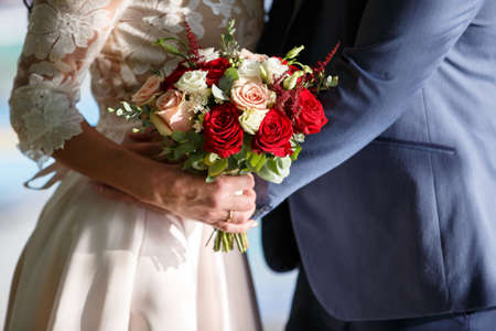 beautiful young bride with long dark hair and a long white wedding dress holding a bridal bouquet of bright red rosesの写真素材