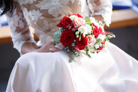 beautiful young bride with long dark hair and a long white wedding dress holding a bridal bouquet of bright red rosesの写真素材