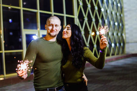 Christmas holding bengal burning sparkler light. Outdoor portrait of young beautiful happy smiling couple posing on street.young couple with Bengal fire in the darkの写真素材