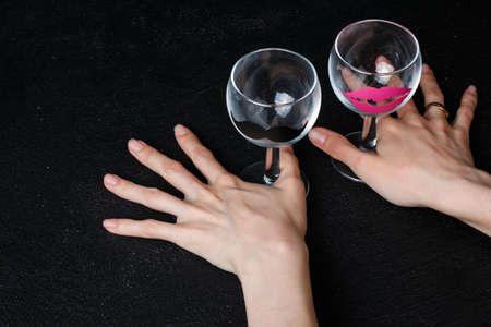 Wine glasses with stickers in the form of female lips and man's mustache in hands on a black backgroundの写真素材