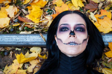 portrait of a young beautiful girl lying on the rails amidst a yellow autumn foliage. she wears a black dress, a dramatic make-up on her face. Dramaの写真素材